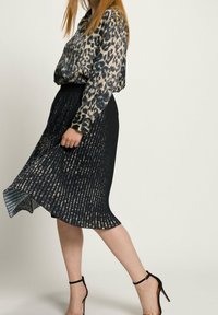 Blusa a stampa leopardata con maniche lunghe, abbinata a una gonna nera plissettata. La gonna presenta strisce verticali e una texture morbida. Tacchi alti neri.