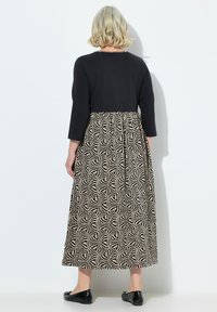 Černý top s dlouhým rukávem a potištěnou sukní po kolena v béžových a černých geometrických vzorech. Vzhled doplňují ploché černé boty.