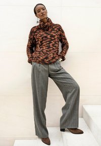 Gebreide trui in donkere tinten met oranje vlekken, met een col. Gecombineerd met grijze streepjes wijde broek en bruine haklaarzen.