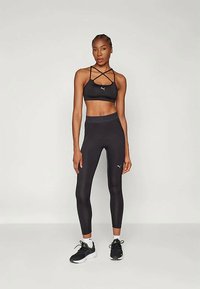 Μαύρη αθλητική εμφάνιση με αθλητικό σουτιέν με τιράντες και κολάν ψηλής μέσης. Το υλικό είναι λείο με διακριτική γυαλάδα, τονισμένο με λογότυπο.