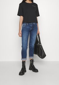 Svart avkortad t-shirt, blå tajta jeans med uppvikt fåll, och svarta snörade kängor med nitar. Bär en stor svart väska.