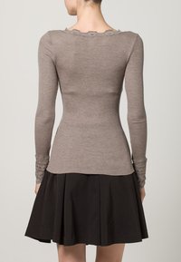 Rebrasti top dugih rukava u svijetlo smeđoj boji, sa valovitim izrezom i čipkastim detaljima na manžetnama, u kombinaciji s crnom suknjom na zvono.