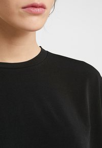 Svart crewneck t-shirt tillverkad av en mjuk bomullsblandning; har korta ärmar, en avslappnad passform och en enkel design utan synliga mönster.