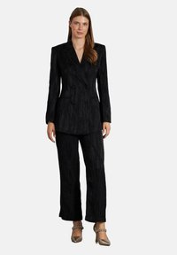 Blazer negro de doble botonadura con tejido texturizado y pantalones de pierna ancha a juego. El conjunto presenta botones en la parte frontal y un corte entallado.