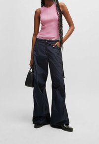 Top a maniche corte rosa fitted con scollatura tonda abbinato a pantaloni baggy in nylon blu navy. Il modello porta una piccola borsa nera e indossa stivali neri.