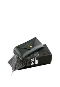 Portafoglio in pelle nera con chiusura a scatto dorata, posizionato su una scatola nera con un motivo logo geometrico bianco e un panno per la pulizia.