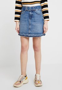 Džínová sukně s páskem, modrý praní, ořezané okraje a pět kapes. V kombinaci s vícebarevnými teniskami s robustní podešví.