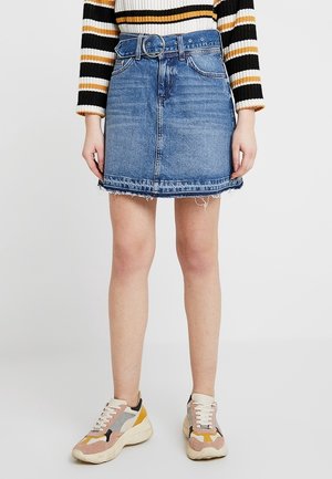 Jupe en denim avec ceinture, délavage bleu, ourlet effiloché et cinq poches. Associée à des baskets multicolores avec une semelle épaisse.