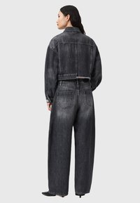 Zwarte denim jacket en bijpassende wijde broek, met een cropped ontwerp, versleten textuur en subtiele details op de achterzakken.