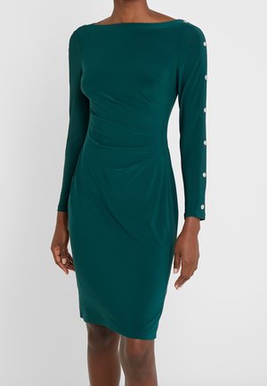 Teal aansluitende jurk met lange mouwen. Rekbare stof, gladde textuur, met plooidetails en zilveren knoopaccenten langs de mouwen.