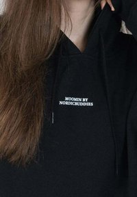 Musta huppari, jossa on etupussit, nyörit ja valkoinen teksti: "MOOMIN BY NORDICBUDDIES" keskellä rintaa.