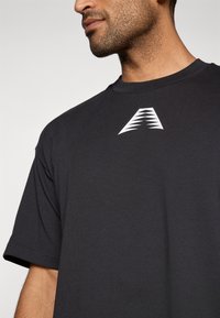 Čierne tričko s krátkymi rukávmi s bielym štýlovým logom na hrudi, vyrobené z jemného materiálu s klasickým strihom.