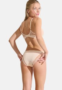Ensemble de lingerie beige avec des accents en dentelle ; le soutien-gorge dispose de bretelles réglables et d'une fermeture à agrafe ; culotte assortie avec des détails en dentelle sur les côtés.