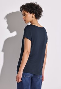 Top de manga corta azul marino hecho de una tela suave, con un corte holgado y un escote amplio, combinado con jeans de color azul claro.