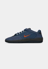 Modrá sportovní bota s texturovaným síťovaným svrškem, semišovými akcenty a oranžovým logem Nike; má polstrovanou černou podrážku a systém šněrování.