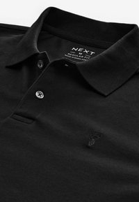 Black polo shirt made of textured fabric, featuring a collar, three buttons, and a subtle embroidered logo on the chest.