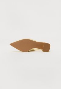 Beige kengät, joissa on terävä kärki ja matala, suorakulmainen korko, makaa kyljellään valkoisella taustalla.