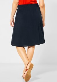 Námořnická sukně ve tvaru A s elastickým pasem, střední délka, lehká tkanina, doplněná hnědými sandály na řemínky, hladká textura.