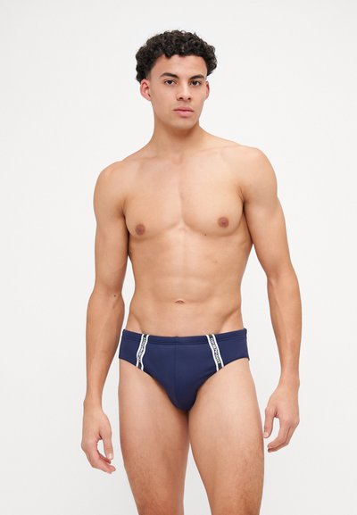Caleçons de bain navy avec un design ajusté, une bordure blanche contrastante le long de la taille et un tissu lisse et extensible pour le confort.