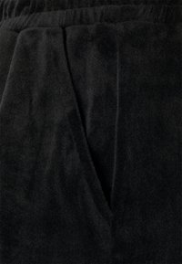 Black fleece fabric with a soft, textured surface, featuring a relaxed waistband and slanted side pockets for comfort and utility.