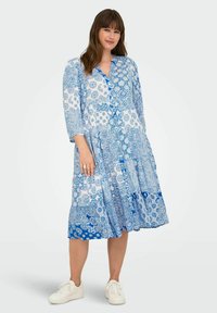 Modra in bela obleka z vzorcem, s tremi četrtinami rokavi, gumbi po sprednji strani in slojeno zasnovo. Nosi se z belimi supergami.