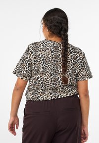 Top a maniche corte con stampa leopardata nei colori beige, nero e marrone, con una vestibilità rilassata. Tessuto liscio con scollo rotondo e capelli intrecciati visibili.