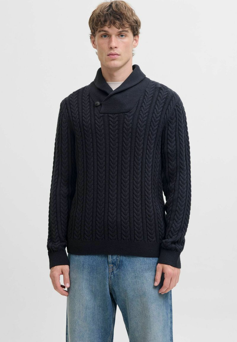 Ciemnogranatowy sweter dzianinowy z wzorem w warkocze, z kołnierzem typu szal i pojedynczym zapięciem na guzik. Połączony z jasnoniebieskimi, luźnymi dżinsami.