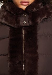 Hnědá péřová bunda s límcem z umělé kožešiny. Obsahuje přední zip a kovové patentky. Hladký povrch s hebkým, měkkým vzhledem.