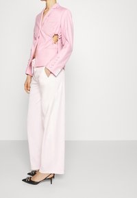 Roze blazer met uitsnijdingen, enkele zak en knopenaccenten. Gestyled met lichtroze broeken en zwarte hakken met een spitse neus.