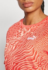 Punainen kuvioitu t-paita, jossa on pyöreä pääntie ja aalto- sekä suomukuviot; edessä valkoinen Puman logo.