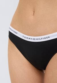 Μαύρο βαμβακερό εσώρουχο με λευκή ελαστική μέση όπου αναγράφεται "TOMMY HILFIGER". Λεία υφή, κλασική εφαρμογή, μεσαίο ύψος.