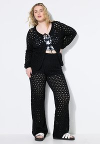 Zwarte gehaakte cardigan en broekset, met opengewerkte structuur, ontspannen pasvorm en gebreide textuur. Gecombineerd met een cropped top en sandalen.