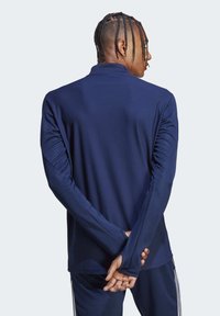Maglietta atletica a maniche lunghe blu navy con tessuto testurizzato, caratterizzata da un colletto alto e una vestibilità slim. Le mani sono posizionate dietro la schiena.