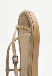 Beige nilon sandaalit, joissa on nahkainen pohja, tasainen kumipohja ja metallinen solki nilkkaremmin yksityiskohtana.