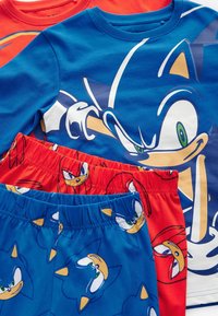 Blaue und rote Schlafanzüge mit Cartoonfiguren. Das blaue Shirt hat ein großes Grafikdesign, während die Shorts mit wiederholten Charaktermustern versehen sind.