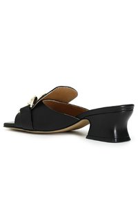 Mules noires à talon avec un bout ouvert pointu, en cuir lisse, et un talon bloc distinctif. Présente un accent décoratif sur le dessus.