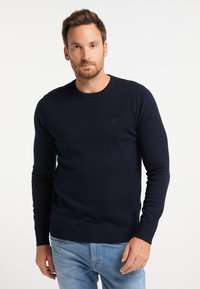 Sötétkék kötött pulóver kerek nyakkivágással, bordás mandzsettákkal és alsó résszel. Diszkrét logó részlet a mellen, puha, textúrált anyagból.