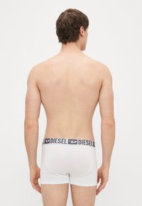 Valged bokserpüksid musta Diesel logo vöökohaga. Kangas näib sile ja vormiv, ilma täiendavate mustrite või aktsentideta.