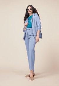 Ensemble de survêtement bleu clair avec un sweat à capuche zipé et un pantalon fuselé, assorti à un T-shirt turquoise orné d'un motif en forme de cœur. Chaussures beiges avec des nœuds.