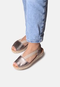 Metalliska bronsefärgade espadrillosandaler med öppen tå, elastiska remmar och sula omsluten av jute. Kombinerat med ljusblå jeans.