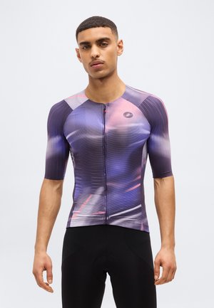 Mann trägt eng anliegendes Radtrikot mit kurzem Ärmel in lila-pinkem Farbverlauf und schwarze Radhose vor einfachem Hintergrund.