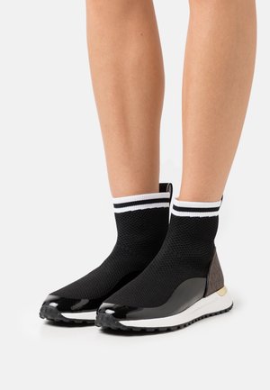 Sorte strikkede ankelstøvler med en sort lakeret tå, hvid stribet manchet og brun tekstureret detalje på hælen. Letvægts, sporty design.