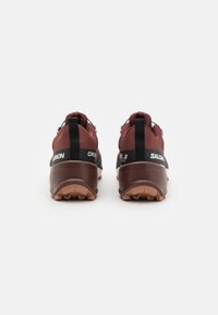 Röda och svarta terränglöparskor med en strukturerad ovandel, förstärkt häl och gummiyttersula med greppmönster för bättre fäste.