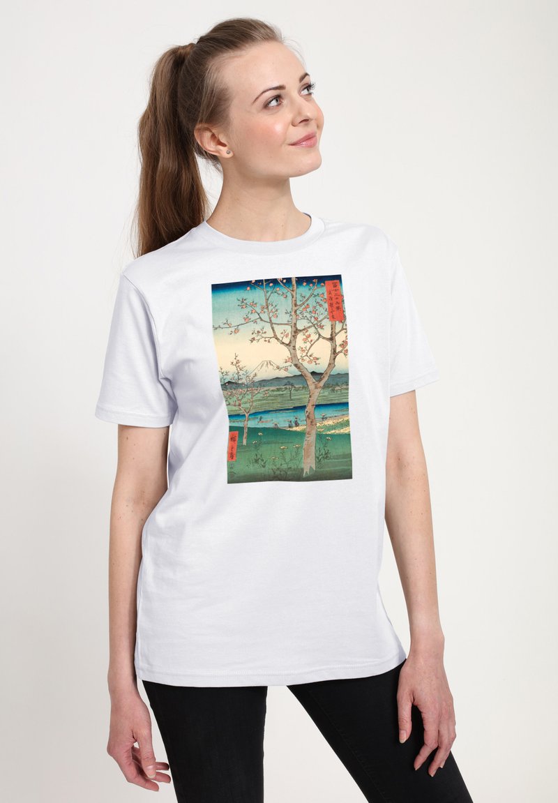 Bílé tričko s potiskem krajiny s stromy, vodou a horami. Design kombinuje odstíny modré, zelené a růžové.