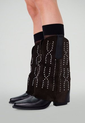 Bruine suède enkellaarsjes met zilveren studs in een decoratief patroon, met een zwarte leren hak en puntige neus.