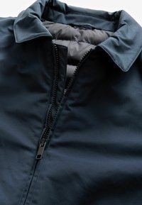 Jachetă albastră marină cu un exterior neted, guler pliant și închidere cu fermoar complet. Interiorul are o căptușeală gri căptușită pentru izolație.