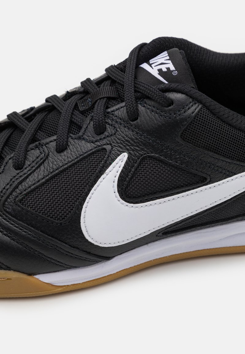 Chaussure de sport noire avec une tige en cuir texturé et en mesh. Présente un swoosh Nike blanc, des lacets noirs et une semelle en caoutchouc avec une accent en gomme.