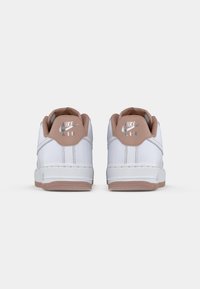 Les baskets Nike Air présentent une tige en cuir blanc, des accents rose doux sur le talon et une semelle extérieure en caoutchouc texturé pour une adhérence optimale.