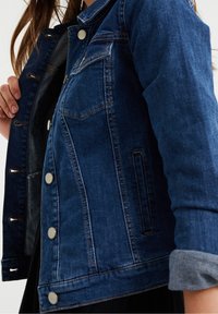 Blå denimjacka med silverknappar och stickningar. Har en klassisk design, bröstficka och uppvikta  ärmar. Texturerad tyg synlig.