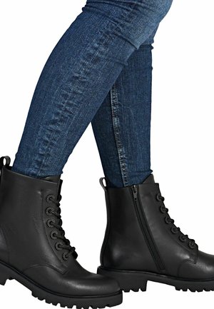 Bottes noires en cuir à bout arrondi, avec un laçage à l'avant, une fermeture éclair sur le côté et une semelle robuste, portées avec un jean skinny bleu foncé.